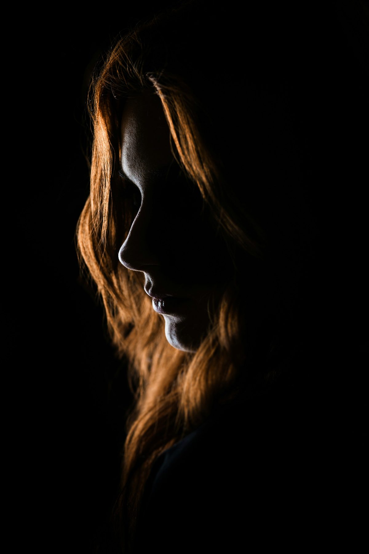 A woman in profile, lit from the side against darkness